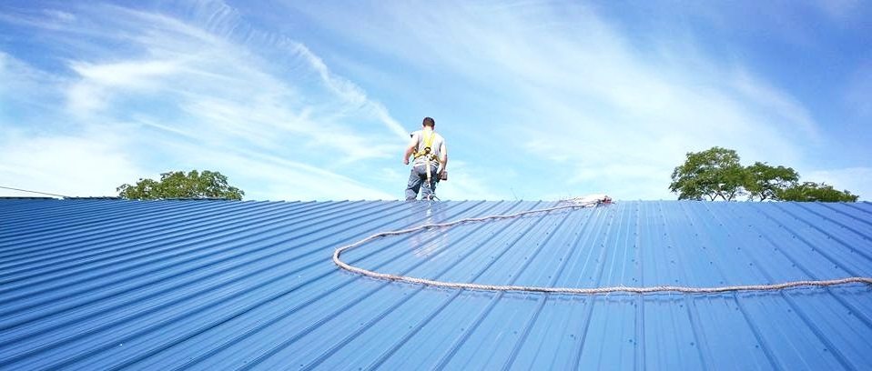 Man with safety harness walking on blue metal roofing
