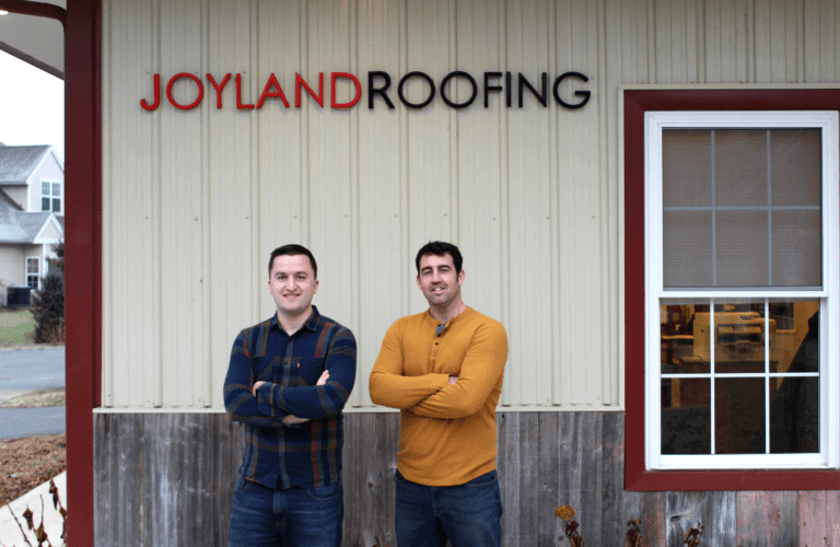 2 employees standing in front of Joyland Roofing building