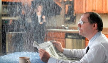 man sitting at table reading a newspaper with water raining on him