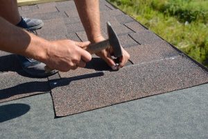 Roofer hammering nails into asphalt shingle