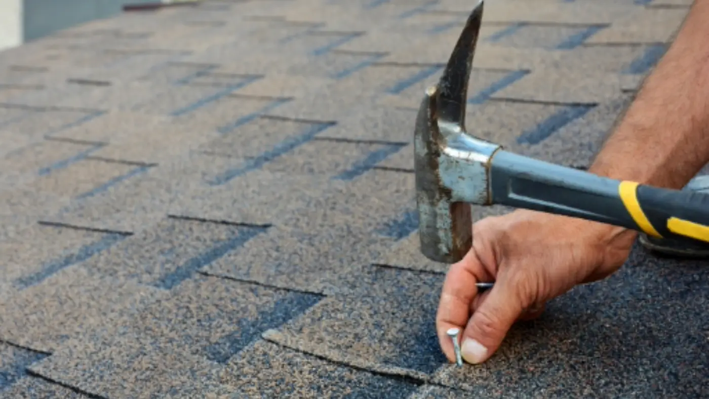 An asphalt roof being installed with a hammer on a commercial property