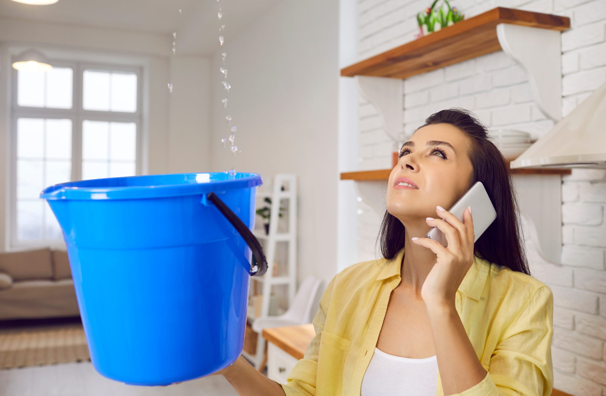 Woman on the phone with blue bucket under leaky roof
