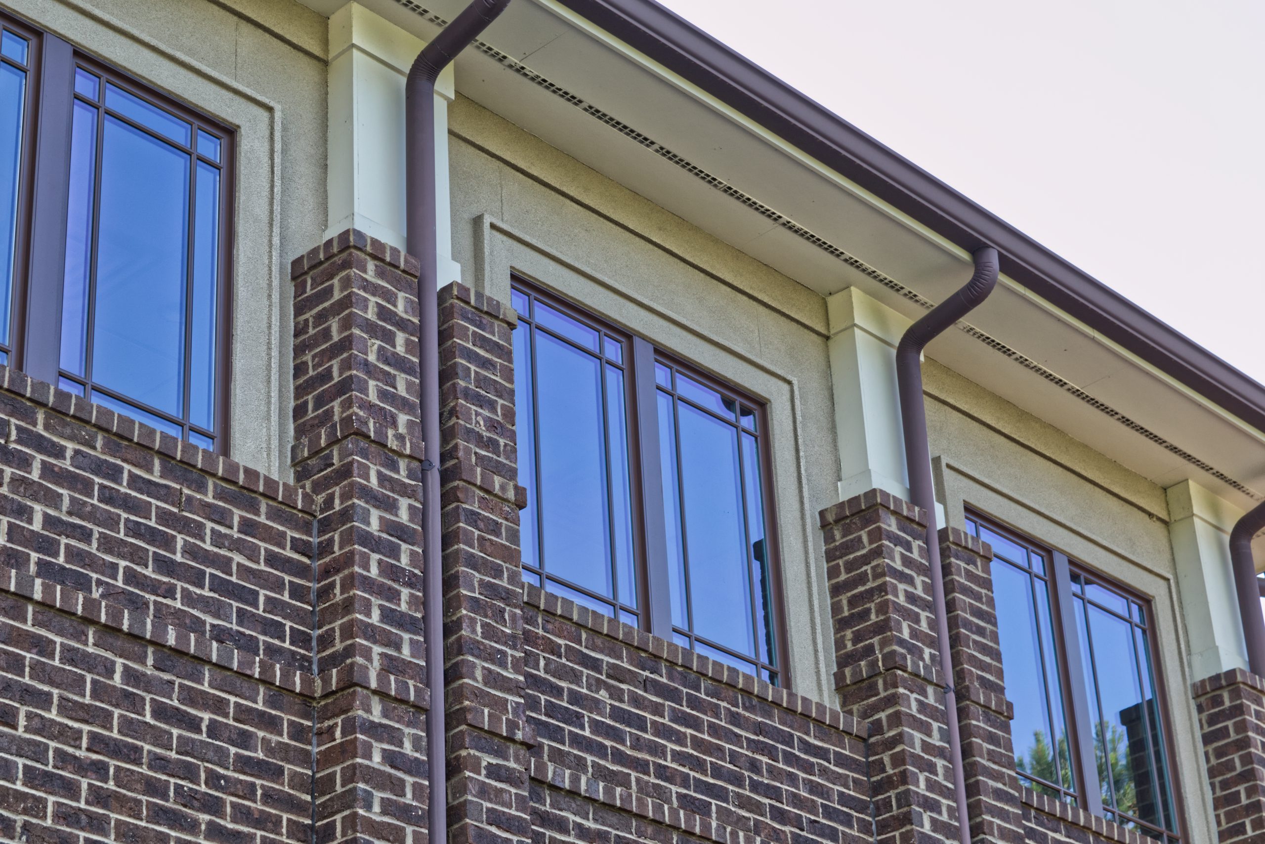 Brown seamless gutters against large brick and stucco commercial building with glass windows