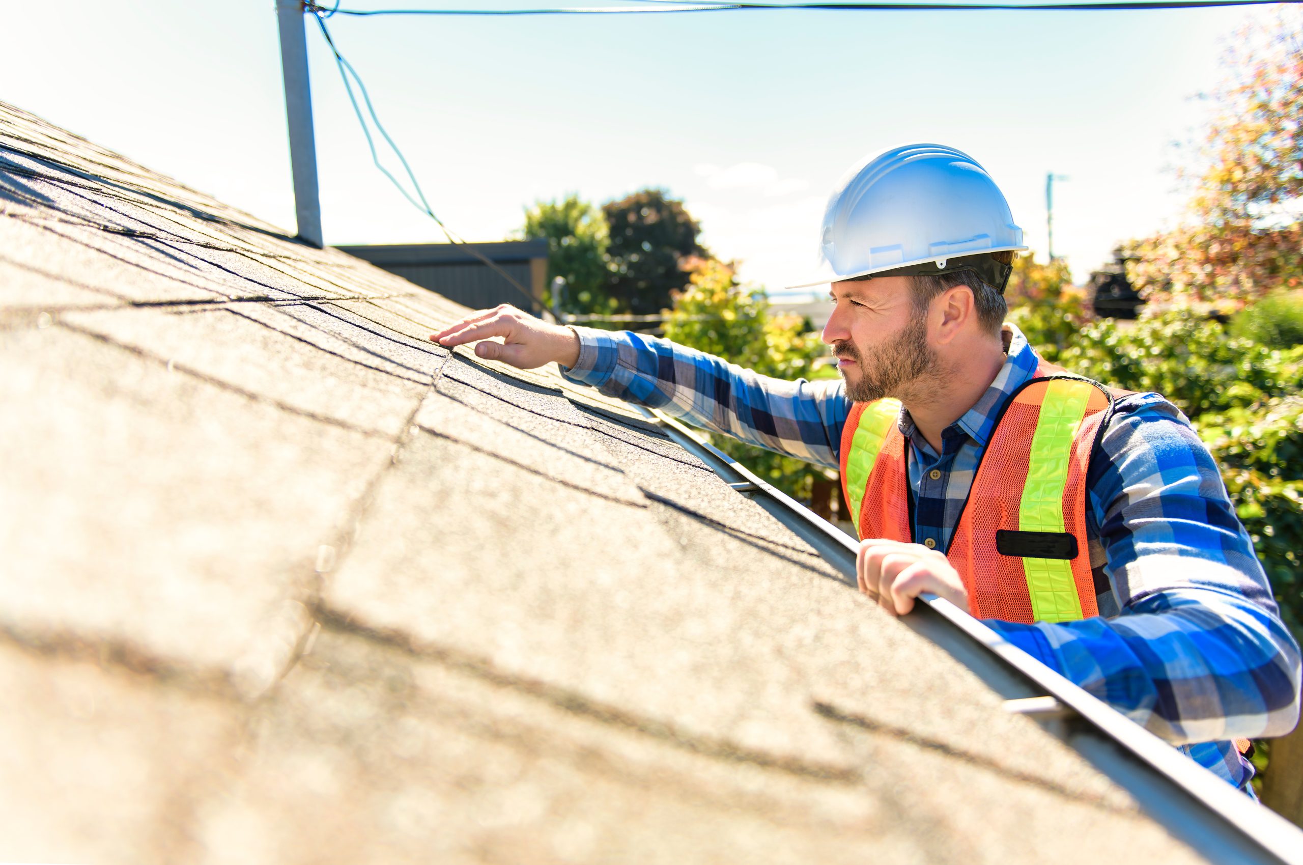 Technician in hard hat inspecting residential asphalt shingle roof
