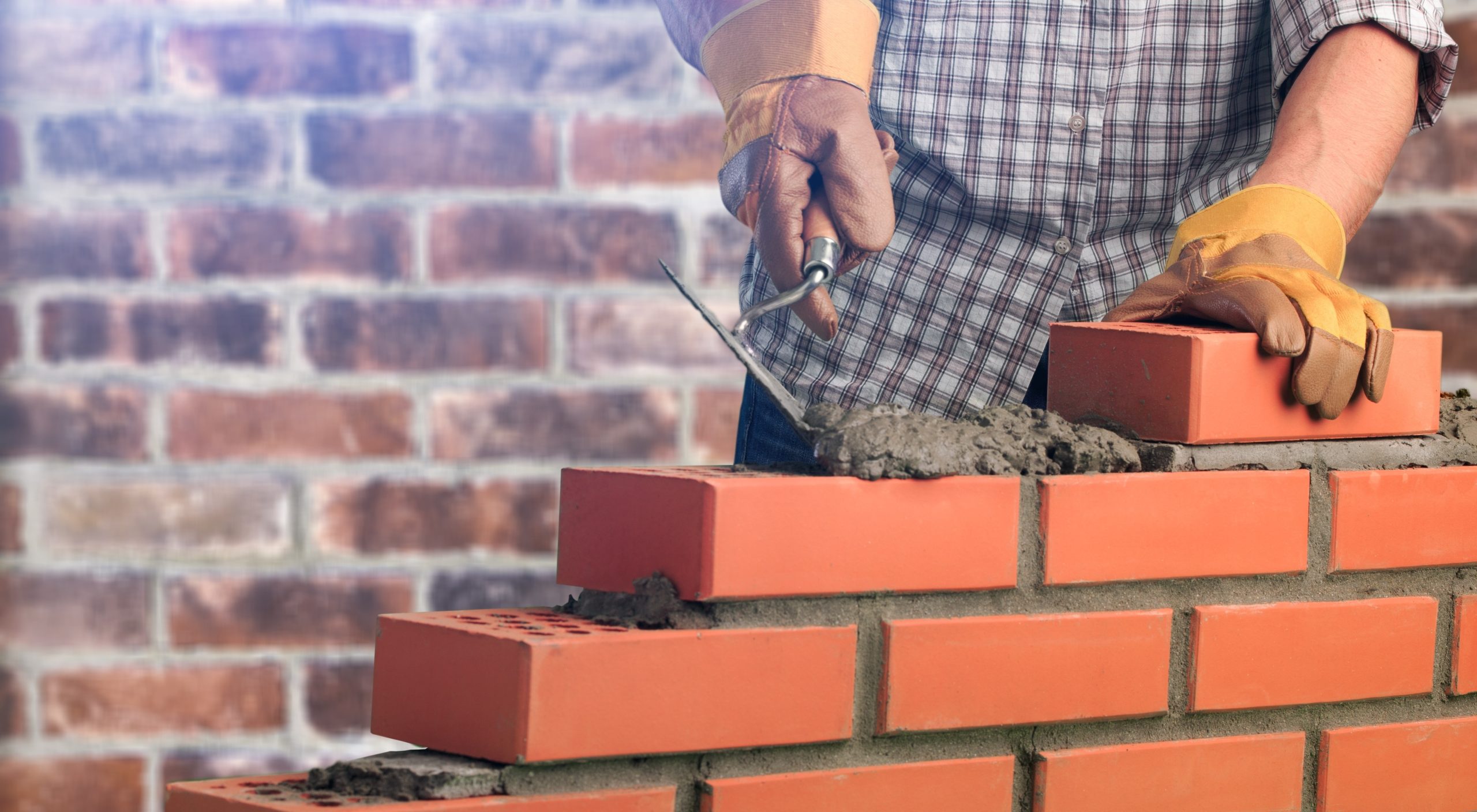 Mason laying red bricks with mortar