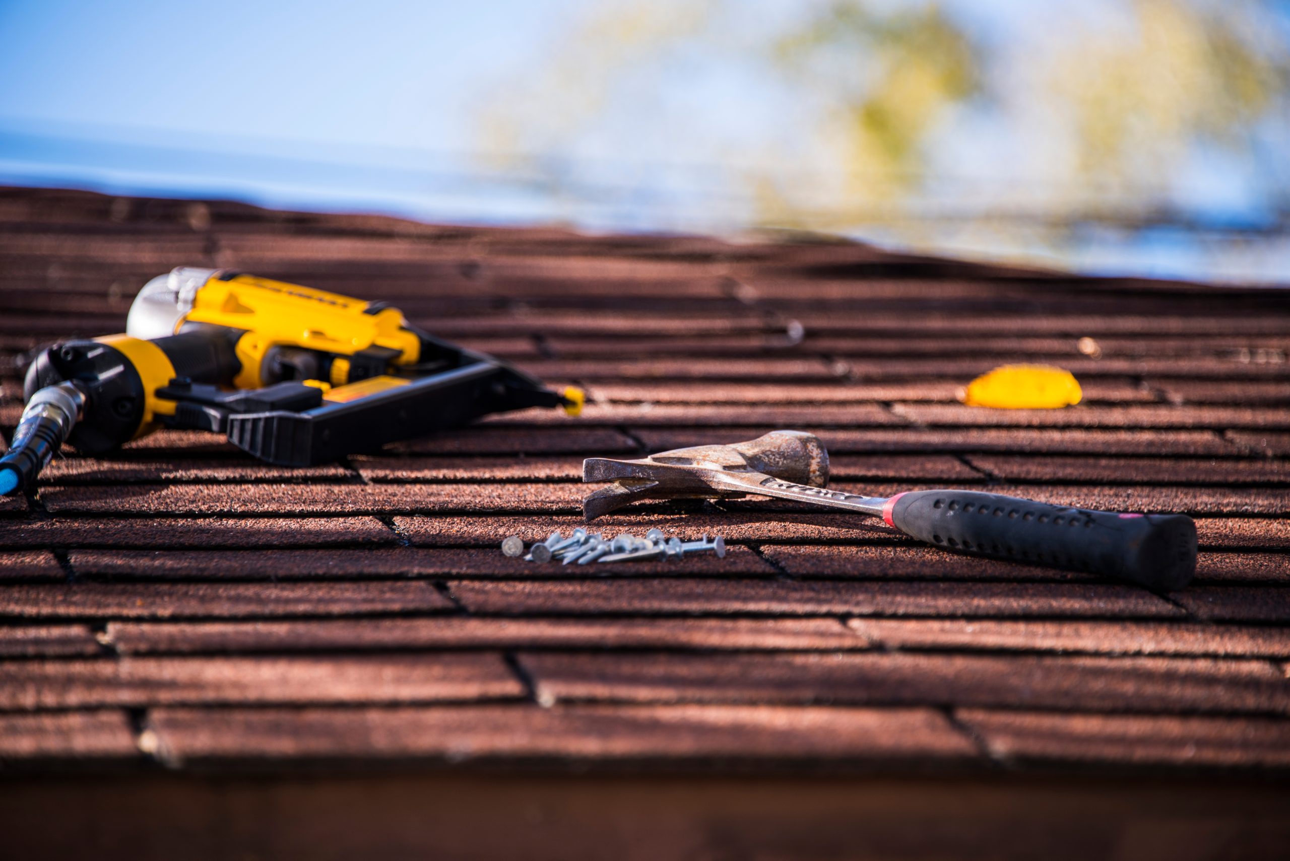 Red asphalt roof shingles with hammer and yellow nail gun